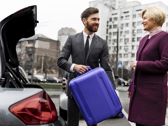 Business travel 2026: guidatore prende valigia signora da mettere nel bagagliaio